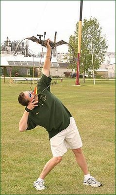 An archer leaning back as he aims an arrow straight up at the pole