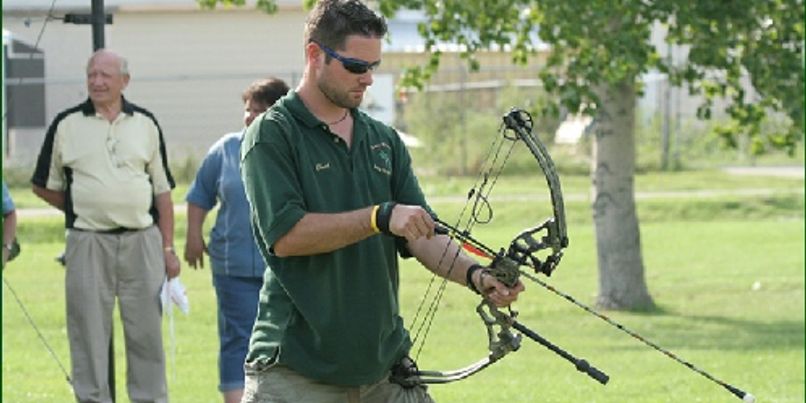 An archer in a green club shirt drawing his bow while other members look on
