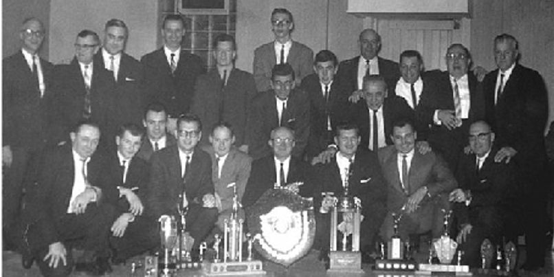 Club members seated and standing behind a table of trophies