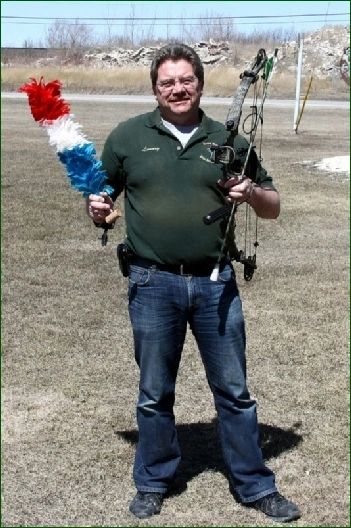 Laurry Lesage standing in a field holding his bow and a red, white and blue feathered King Bird